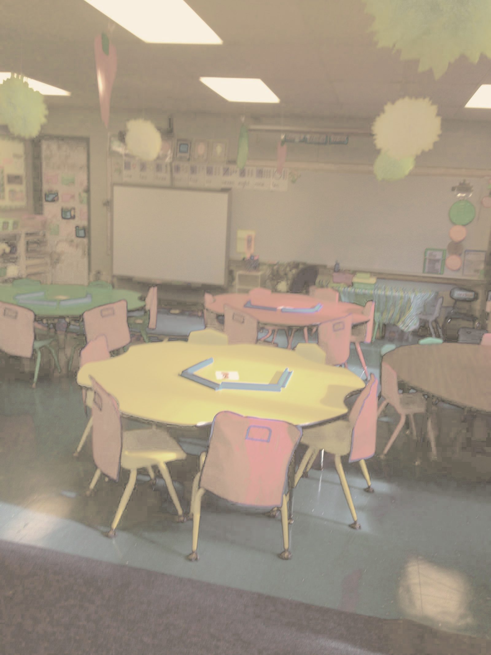 Empty elementary classroom Ali taught in, with colorful square tables and chairs.